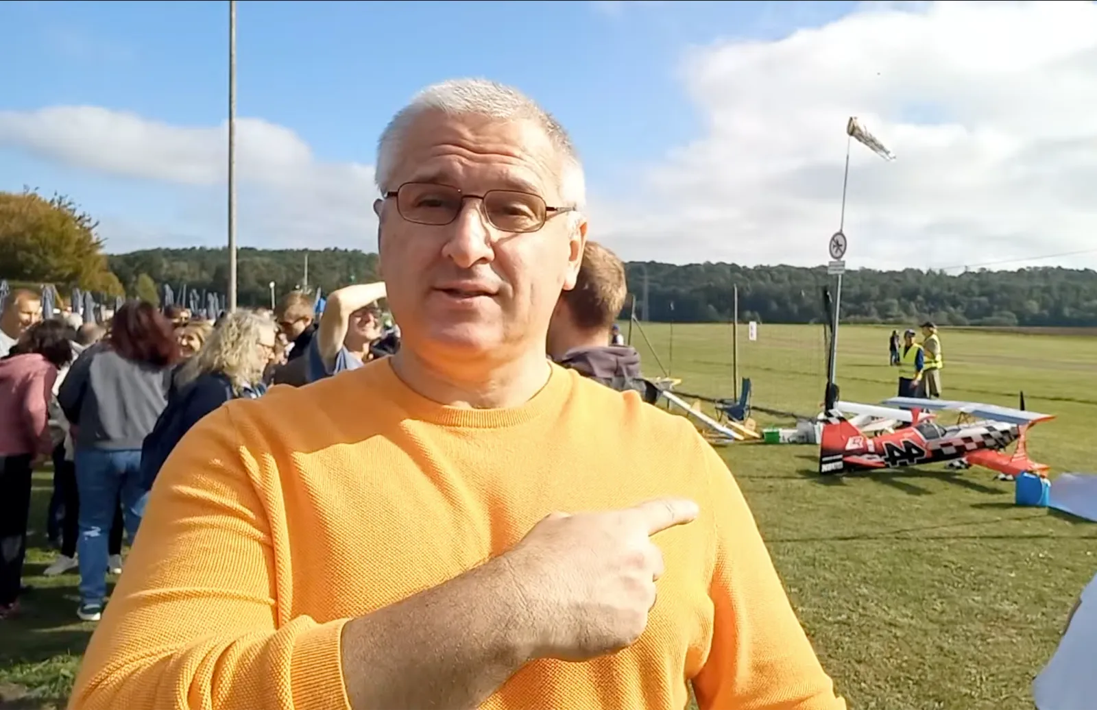 Sergey Raevsky in an orange sweater pointing at a model airplane